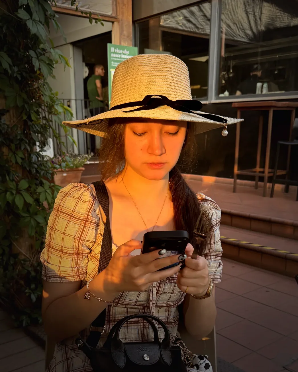 Alexia at a table in the golden hour, in a wide straw hat.