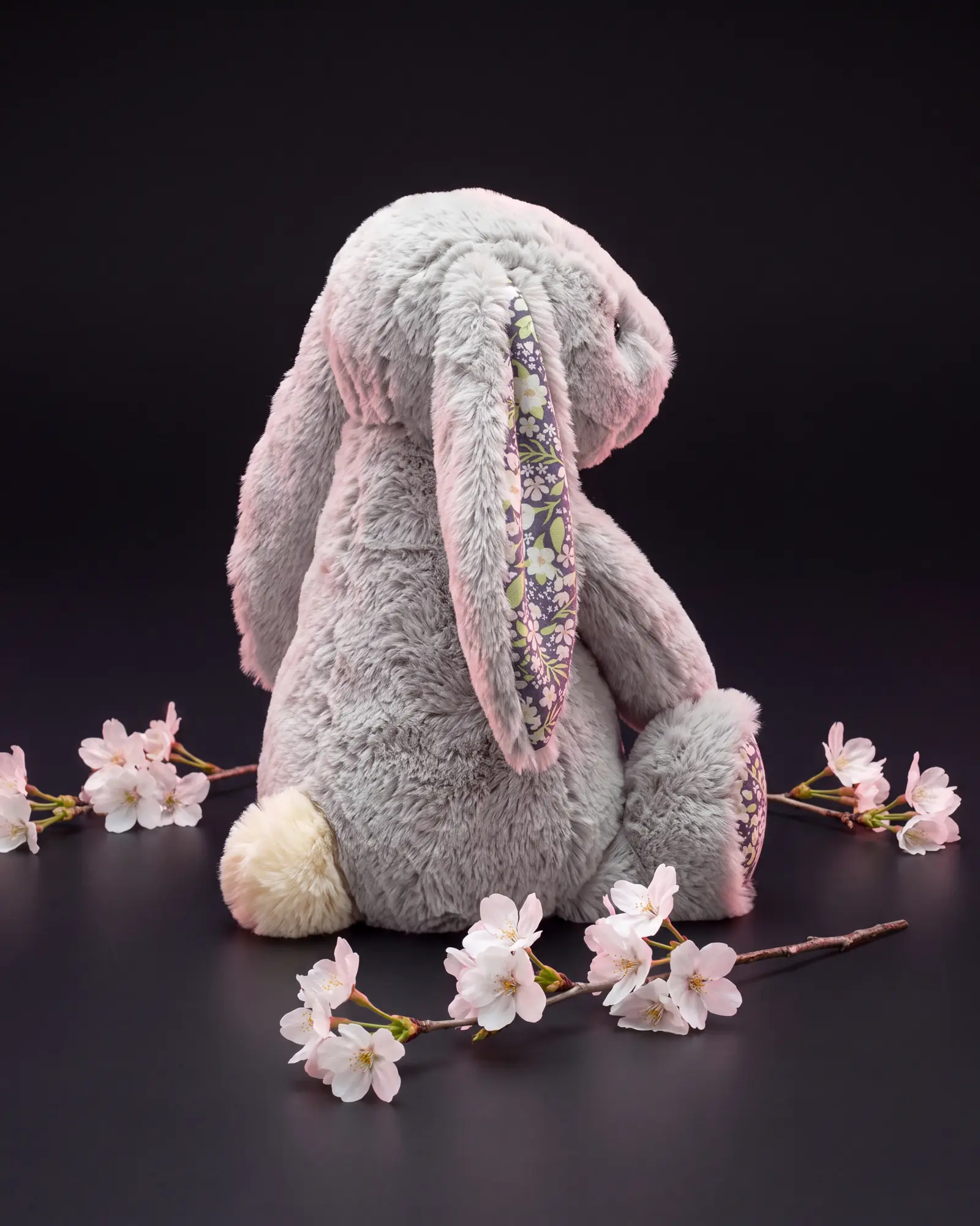 The bunny turned away over its shoulder showing its cream tail, among sprigs of white and pink cherry blossom.