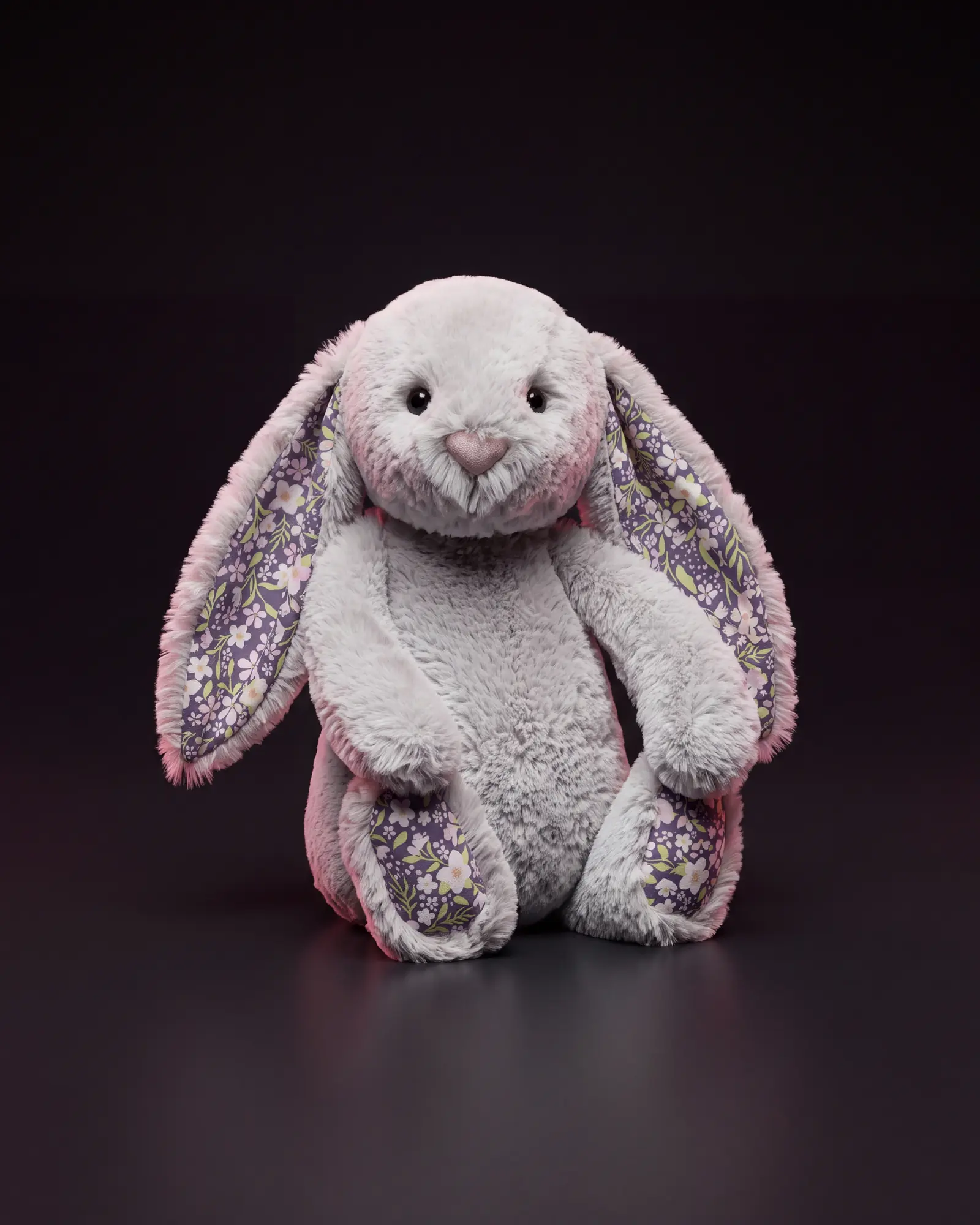 A silver-grey Jellycat bunny with floral-lined ears and floral foot pads, on a dark studio sweep.